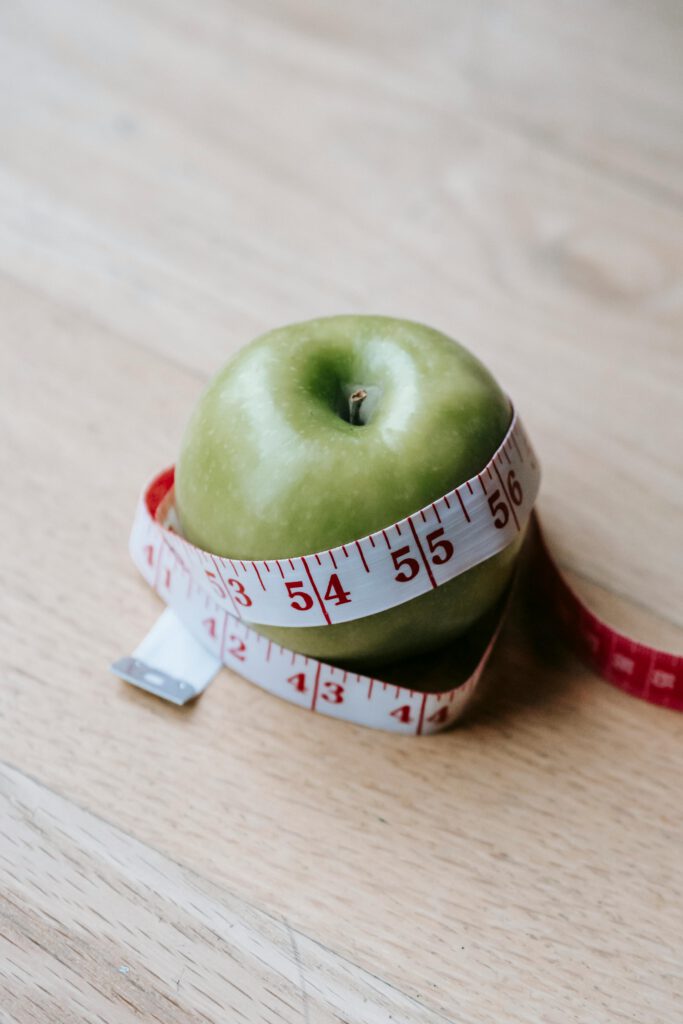 A green apple encircled by a measuring tape, symbolizing diet and fitness goals.